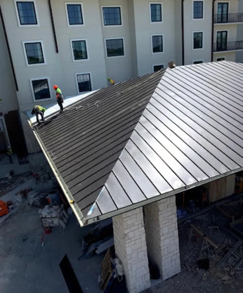 Crew installing standing seam metal roof panels on a commercial project in Elsa